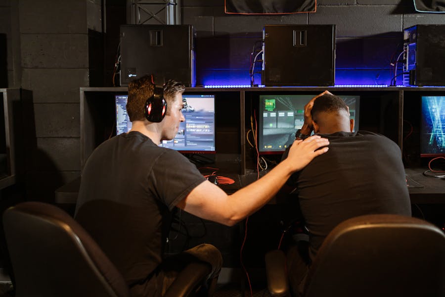 Two players at gaming PCs, one encouraging the other (placeholder)
